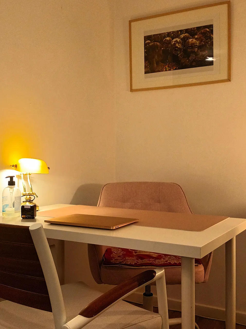 Le bureau du cabinet : lampe de banquier, table blanche et fauteuil rose, sous un tableau encadré